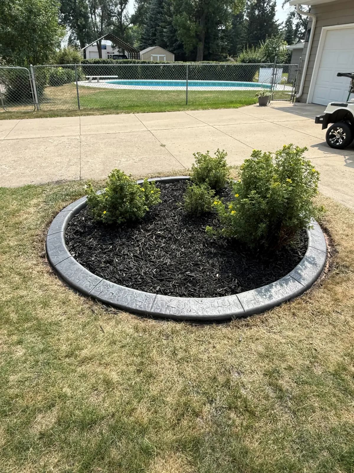 Stamped-concrete curbing wrapping a circular mulch island bed with flowering shrubs in a backyard